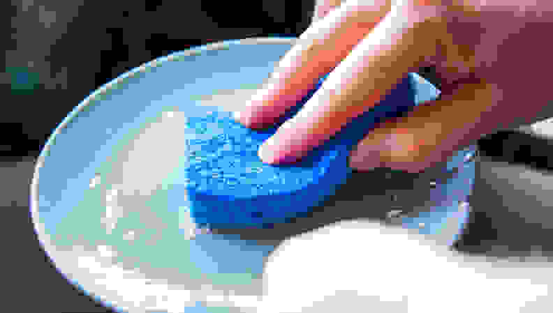 A blue Scotch-Brite non-scratch sponge cleaning a dish