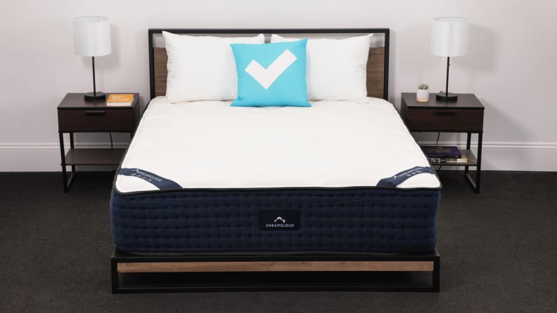 The Dreamcloud mattress appears in a bedroom with bedside tables on either side.