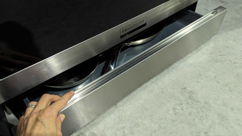 A person pulling a storage drawer in the Frigidaire Gallery stove.