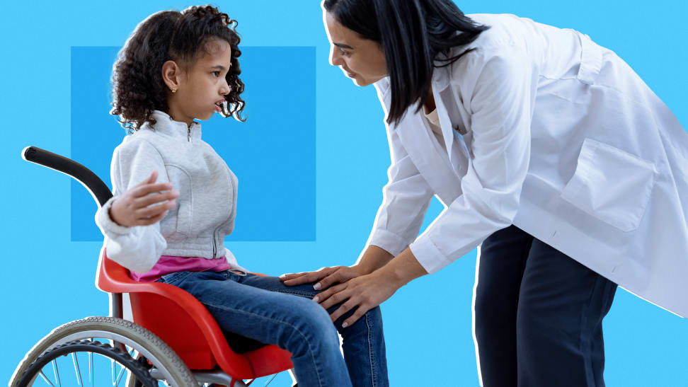 A small child with cerebral palsy sitting in a wheelchair while talking to an adult in a white coat.