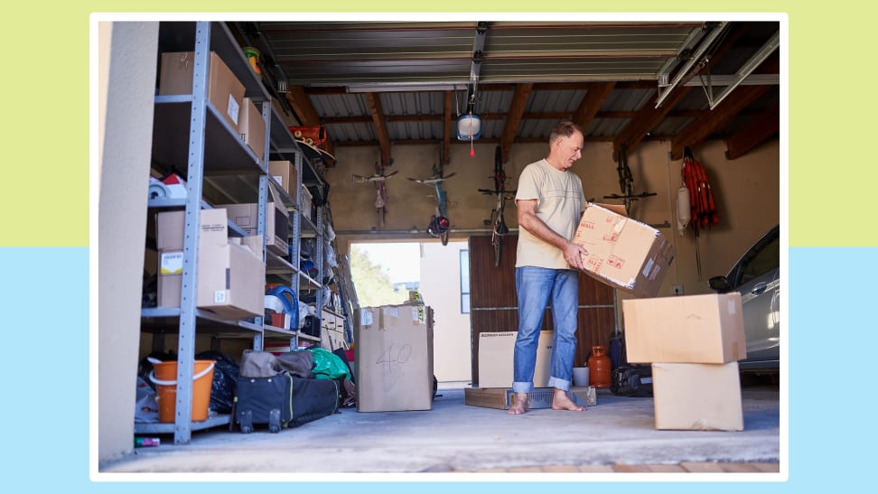 Person standing in garage while holding moving boxes indoors.