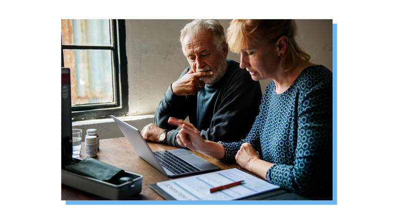 An older couple looking over some paper documents and a laptop.