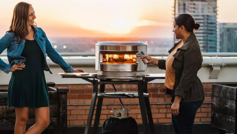 Two people stand on a rooftop with a sunset in the background and a Solo Pi on its stand is between them.