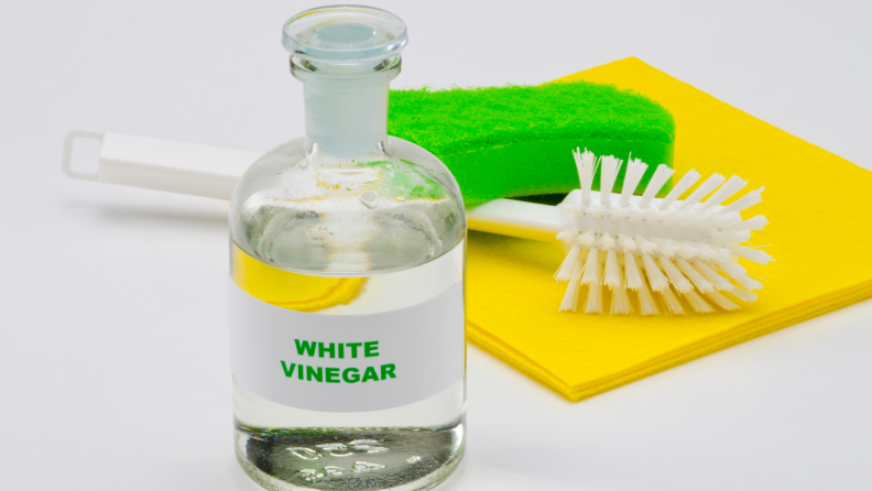 A bottle of white vinegar next to a scrubbing brush and cloth.