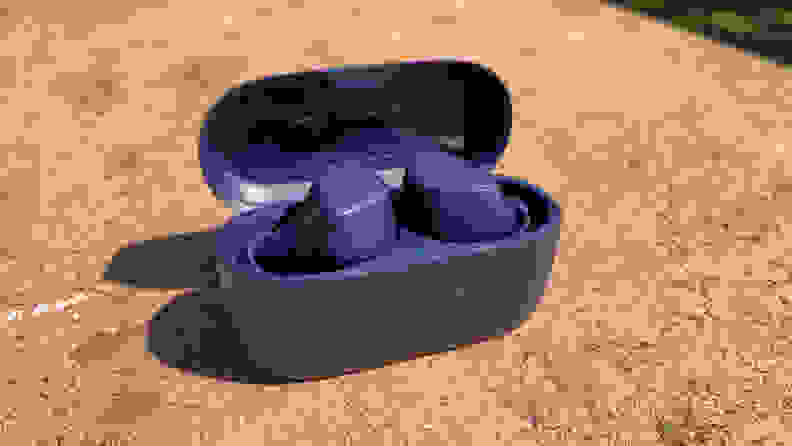 The Jabra Elite 4 earbuds inside a black case on a rock.