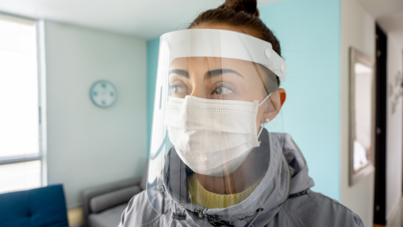 Woman wearing face shield and mask staring off into distance