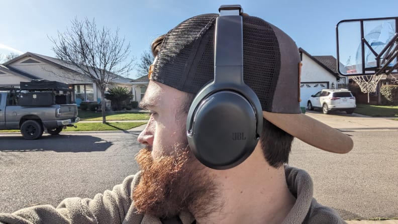 Person turns their head to the side while wearing the JBL Tour One M2 headphones outdoors on a sunny day.