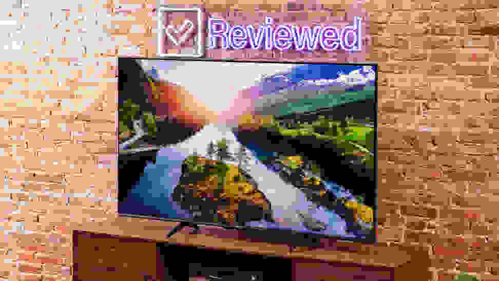 The Hisense U6K displaying a colorful 4K image of a river and a sunset while it sits in front of a brick wall in a living room setting