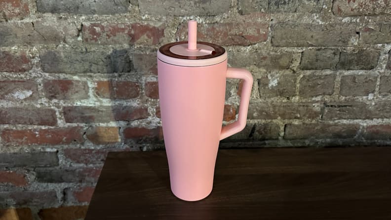 A pink 40 oz. tumbler sitting on a wooden table against a brick background.