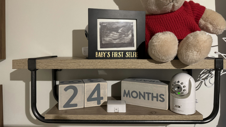 The Infant Optics DXR-8 PRO baby monitor sitting on wooden shelf next to decorative wooden blocks.