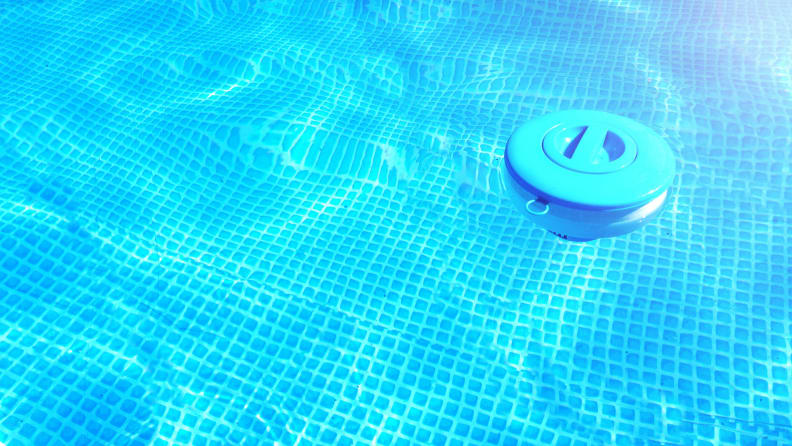 The very clean water of a swimming pool, with a floating chlorine dispenser off to the side of the frame.