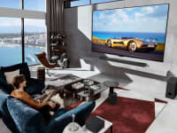 An upscale living room in which the LG M4 wireless OLED TV hangs on the wall in front of a happy viewer and  dog sitting on a couch