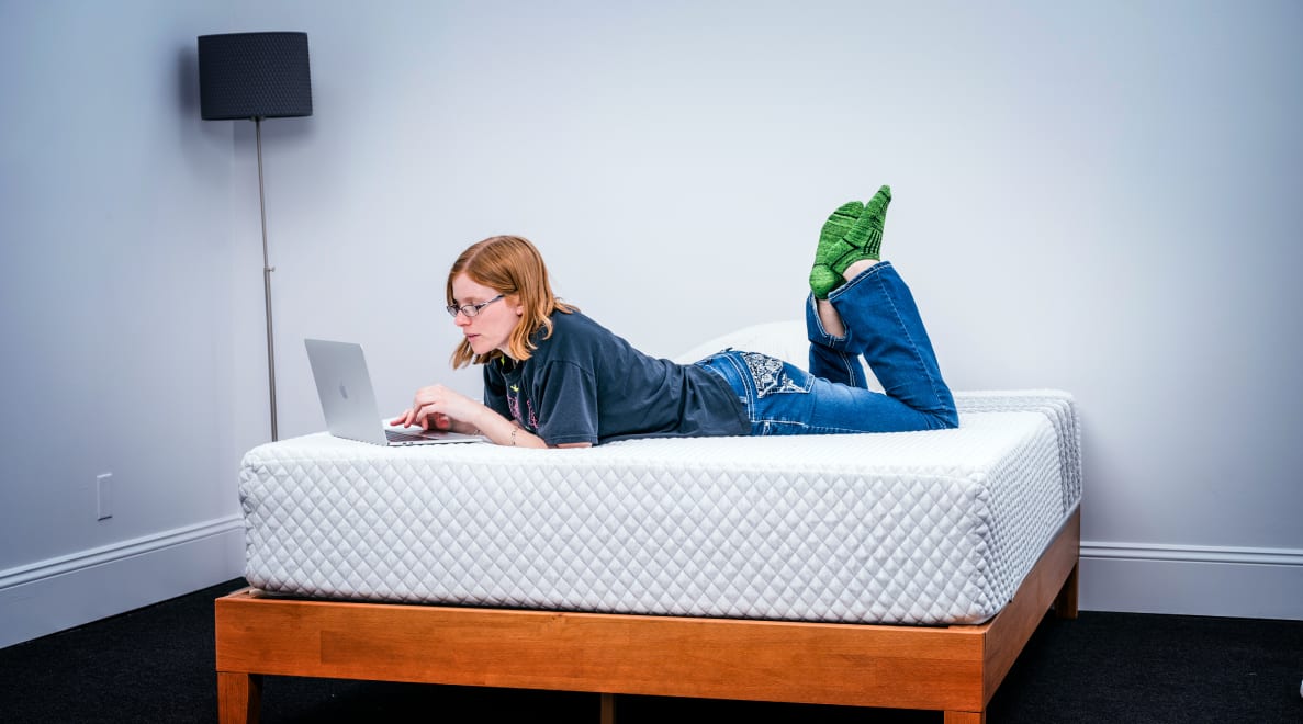 A person laying on their stomach looking at a laptop on the Leesa hybrid mattress
