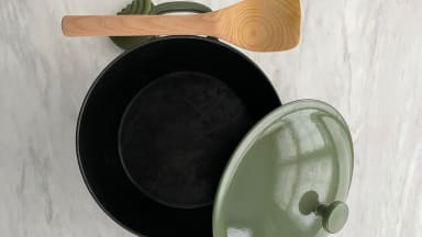 Our Place Cast Iron Perfect Pot in sage green color with lid removed next to wooden spoon.