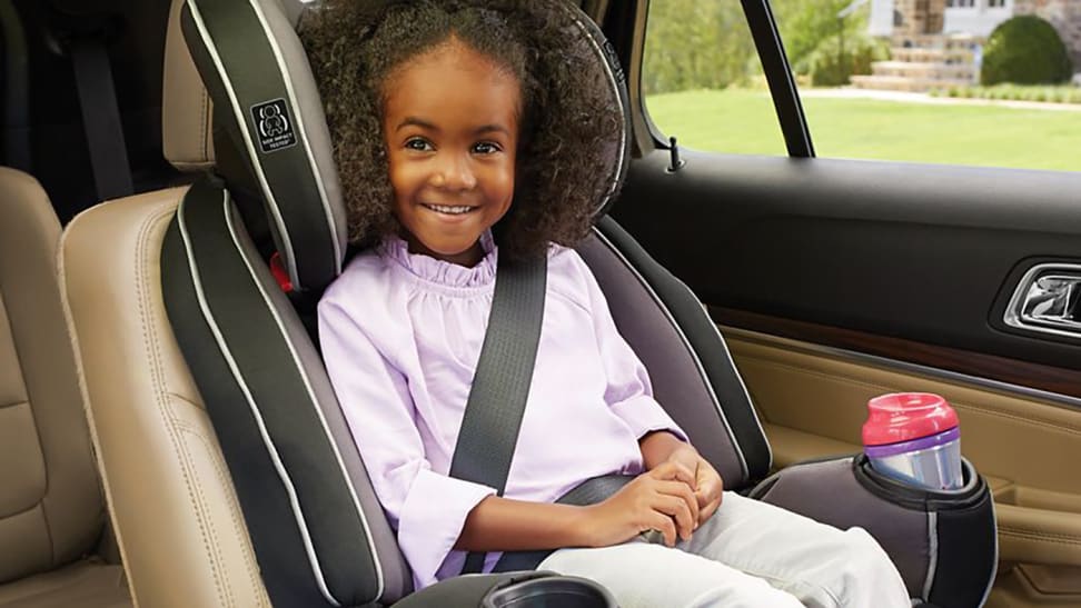 A toddler sitting in a car seat with seat belt buckled across her, and a cup in the cup holder.