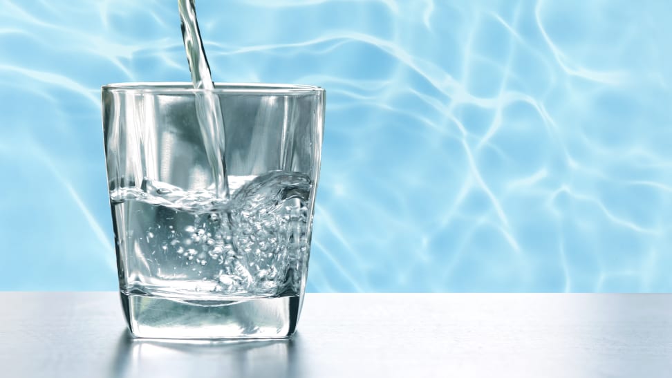 Tap water being poured into a short glass with water in background.