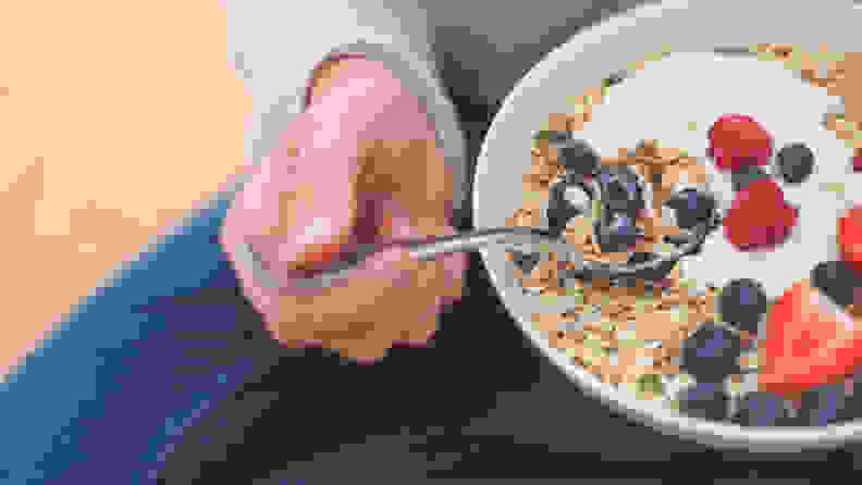 A bowl of yogurt, fruit, and granola being held by someone.