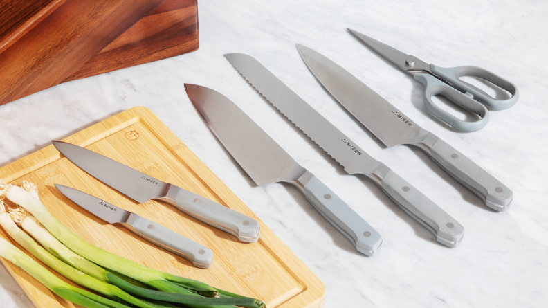 Misen knives laid out on a marble countertop beside a cutting board of scallions