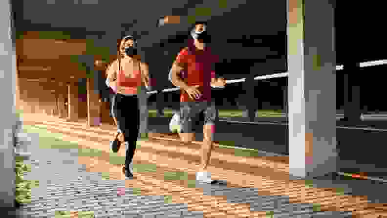 a white couple running side by side wearing masks