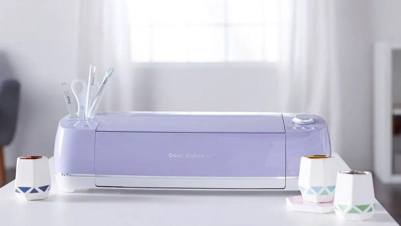 A purple Cricut machine sitting on a white desk in a sunny room.