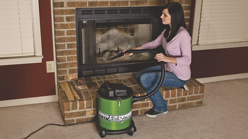 A woman sitting beside a fireplace getting ready to clear it out.