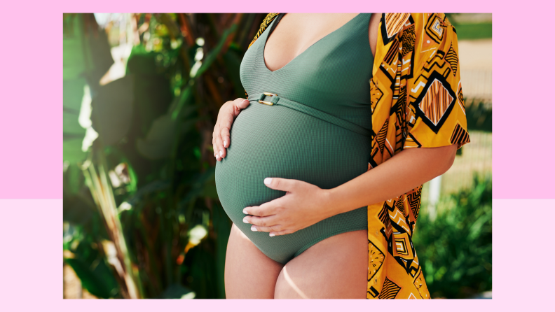 Pregnant person wearing swimsuit while placing hands on bump.