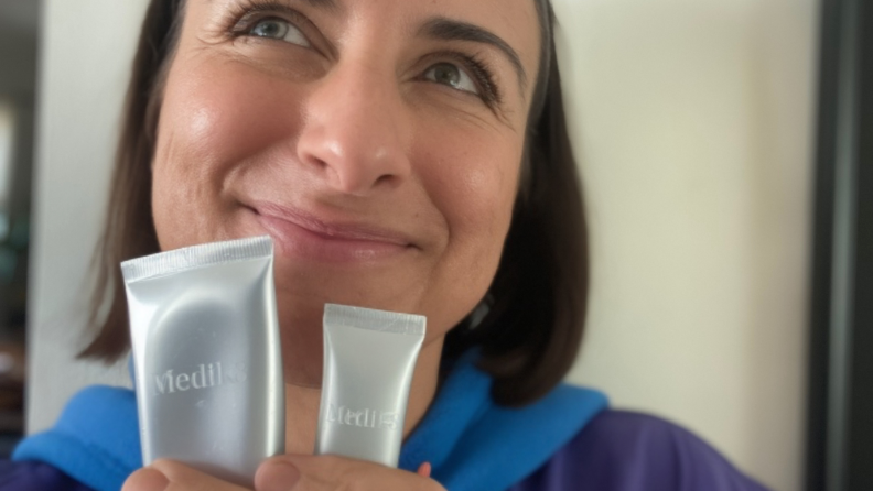 A woman smiles while holding MediK8 products.
