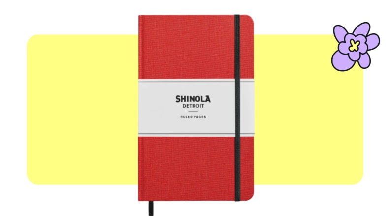 A small, red, hardcover Shinola journal with a reinforced black strap on front.