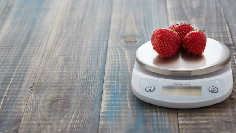 Three strawberries on a small food scale on wooden countertop.