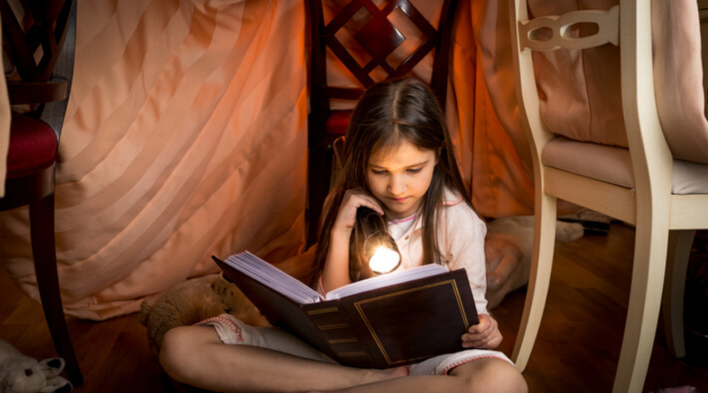 A girl reads a book in a blanket fort