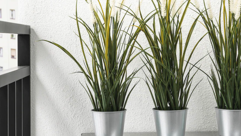 Faux grass plant in metal tins on table.