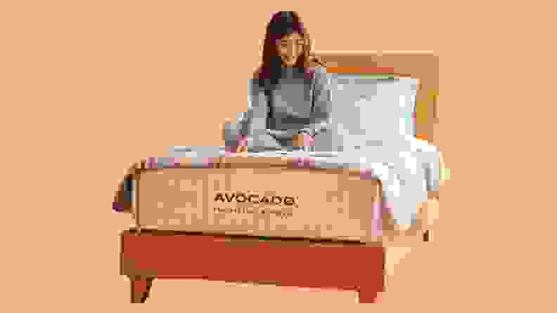 A woman sitting on an Avocado mattress against a peach background.