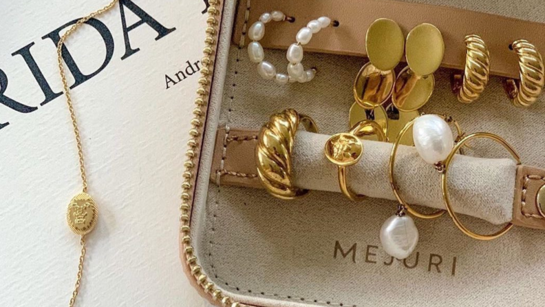 An image of a set of Mejuri jewelry in a display box, including a ridged golden ring, pearl earrings, gold hoops, and more.