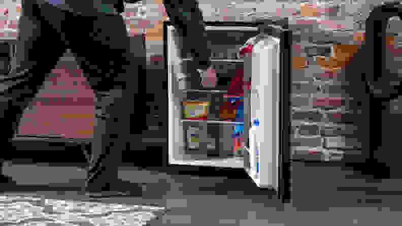 A person reaching into a black mini fridge.