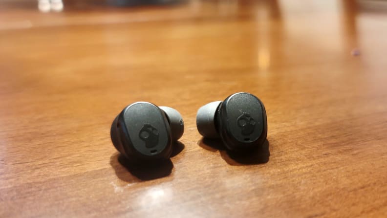The all-black Skullcandy Mod earbuds sit on a wooden cabinet