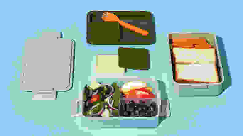 A green Bento box with an assortment of food including a sandwich, fruit, and vegetables.
