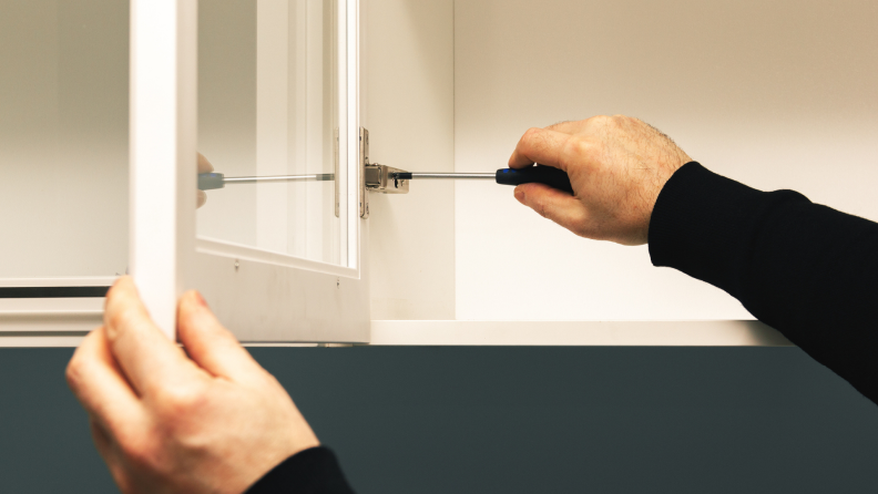 Man using screwdriver to loosen hinge on cabinet door