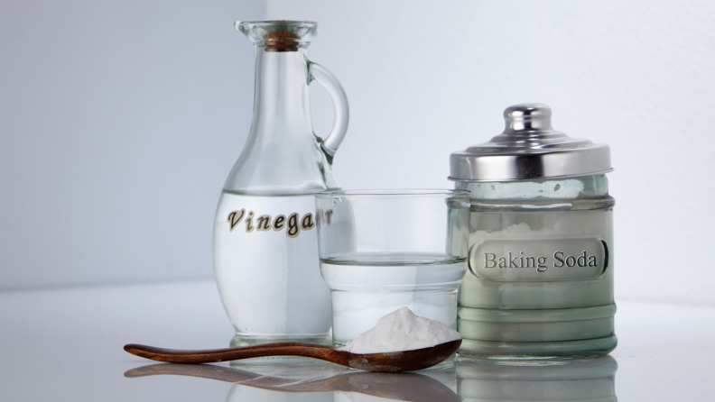 Containers of vinegar, baking soda, a glass of water, and a spoonful of baking soda.