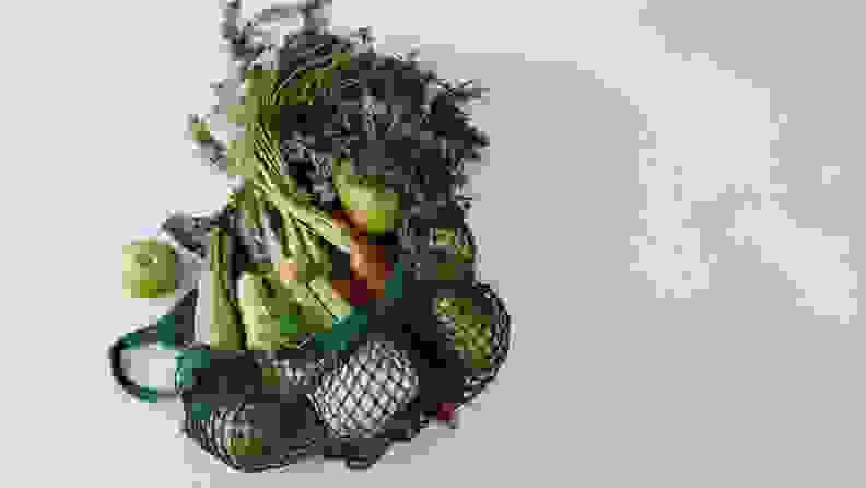 A mesh bag filled with fresh produce on gray background.
