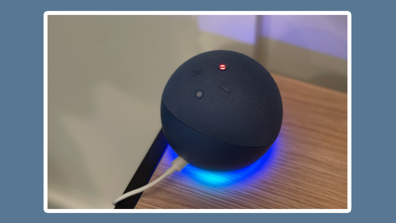 Navy blue 5th generation Amazon Echo Dot virtual assistant speaker sitting on edge of wooden surface indoors with blue LED underneath