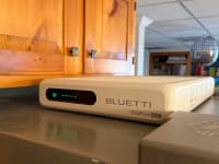 Bluetti FridgePower shown on top of a silver refrigerator in front of wooden cabinets, with a disco ball hanging from the ceiling in the basement shown in the background.