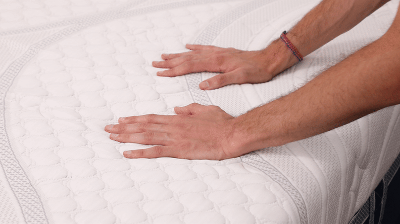 A person squishes a foam mattress with their hands.