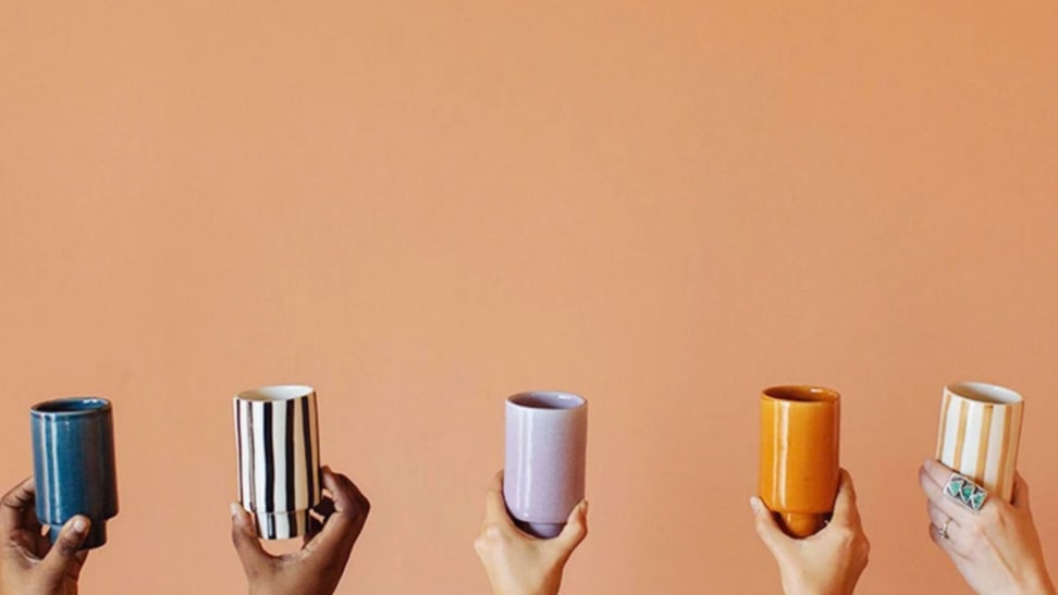 Five hands hold up different colored ceramic cups