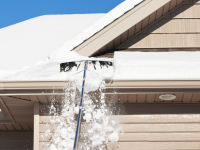一个人用屋顶耙子清除家里的雪。