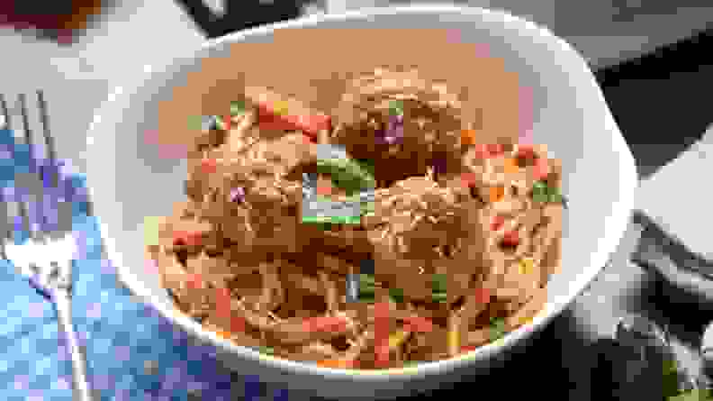 A white bowl of spaghetti and meatballs