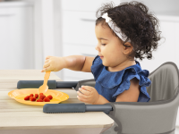 A child eats a snack at the table while seated in a Chicco clip-on high chair.