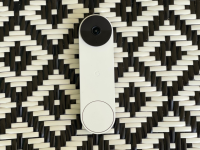 A white video doorbell sits on a black-and-white, diamond-patterned surface