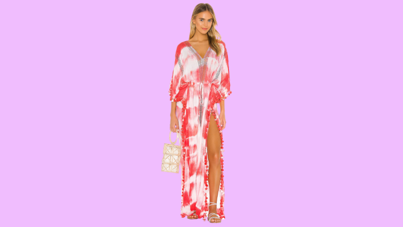 A model wearing a red and white caftan with strappy sandals and a raffia bag.