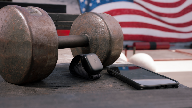 Fitness tracker sitting next to dumbbell and smartphone.