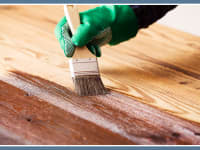 A hand holding a paint brush to stain a deck